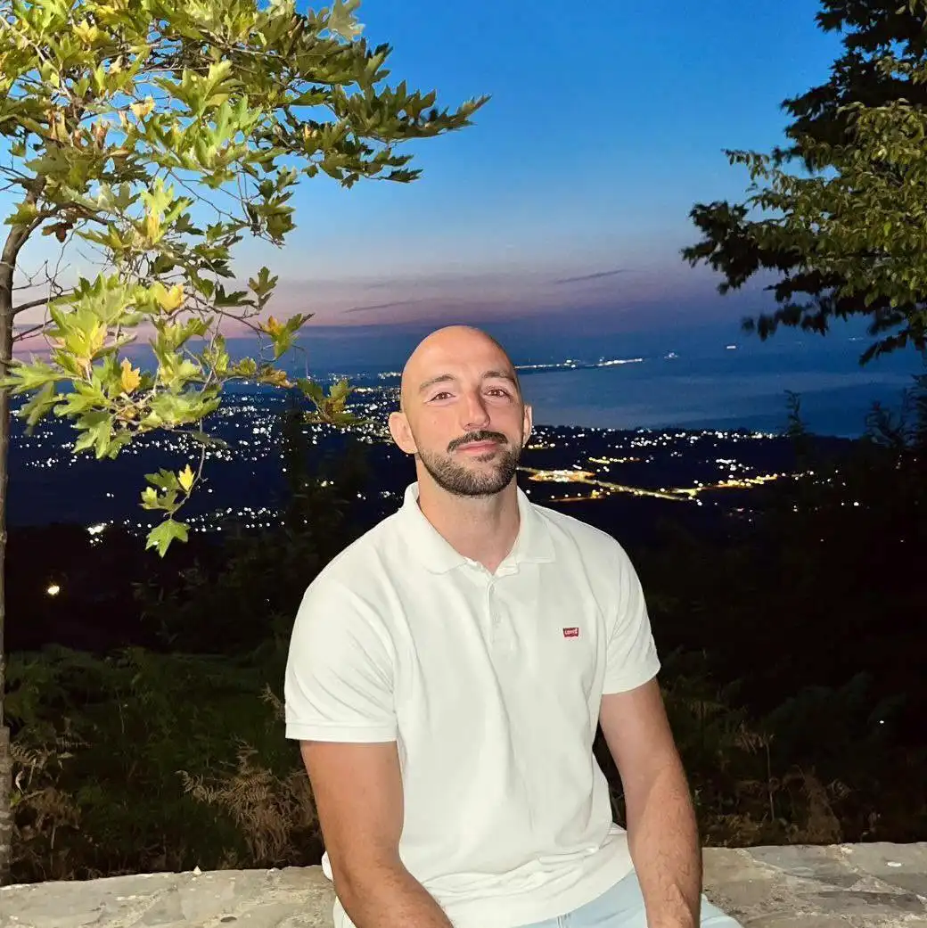 Sotiris at dusk on the stone wall in Palaios Panteleimonas, the lights of the coast below.